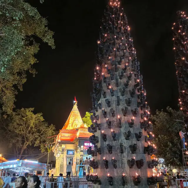रात में प्रज्वलित होता दीप स्तंभ और पीछे रोशनी में नहाया मंदिर (सितंबर 2025)