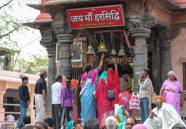 जय माँ हरसिद्धि के बोर्ड के नीचे घंटियाँ बजाते श्रद्धालु